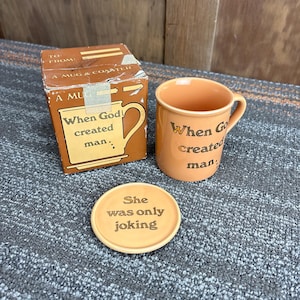 May include: An orange mug, coaster, and box set. The mug and coaster are orange with black text that reads "When God created man." The coaster reads "She was only joking." The box reads "A Mug & Coaster."