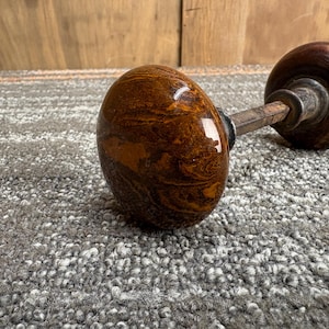 May include: A pair of antique door knobs. The knobs are a rich brown with a marbled pattern and a glossy finish. The connecting rod is metal. The knobs are set against a textured, gray surface.