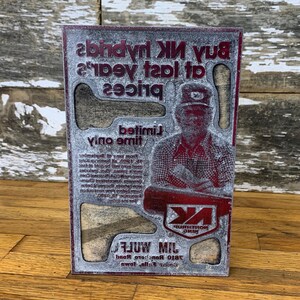Puede incluir: Un letrero rojo y blanco con el texto "Buy NK hybrids at last year's prices. Limited time only." y una imagen de un hombre con un sombrero. El letrero también incluye el texto "810 Rancho Road,  Falls City, Iowa.  MILWULF".