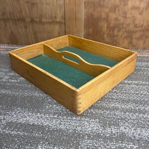 May include: Wooden cutlery tray with a green felt lining. The tray is rectangular with a handle and dividers. The wood has a natural finish. The tray is designed to organize silverware.