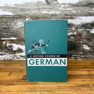 May include: A teal blue book with the title "A Second Course in German" in black text. A black and white illustration of a man walking with an umbrella is on the cover.