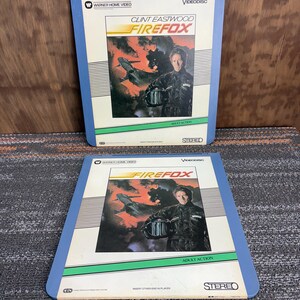 May include: Two vintage "Firefox" Videodiscs featuring Clint Eastwood. The covers have a blue border and display the movie title with a jet and Eastwood's image. The discs are labeled "Warner Home Video" and "Stereo".
