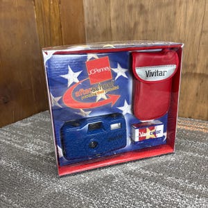 May include: A boxed Vivitar camera set. The set includes a blue camera, a red case with the Vivitar logo, and a roll of film. The box has a patriotic design with stars and the JCPenney logo, with the text "afterschool powering their potential."