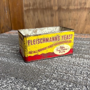 Puede incluir: Lata de levadura Fleischmann's vintage, rectangular con un esquema de color amarillo y rojo. La lata presenta el texto "FLEISCHMANN'S YEAST" y "THE ALL PURPOSE YEAST FOR HOUSEHOLD USE". Un óvalo blanco dice "Take Two Cakes Daily".