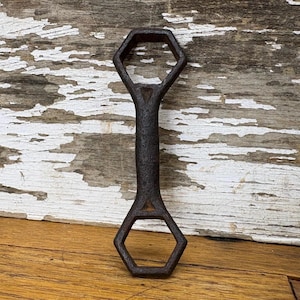 May include: A vintage, rusty, cast iron wrench with two hexagonal openings. The wrench is a dark brown colour and has a worn, aged appearance.