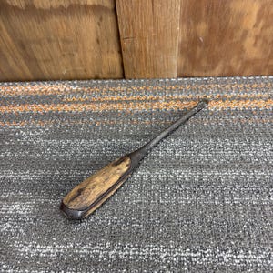 May include: A vintage chisel with a wooden handle and a metal blade. The handle is a light brown color with dark brown accents. The metal blade is a dark gray color. The chisel is lying on a gray and orange striped surface.