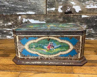 May include: Vintage rectangular tin box with a hinged lid. The box features a blue and cream-colored design with a central oval scene depicting two figures dancing in a landscape. The box has ornate gold-colored trim and a dark brown lid.