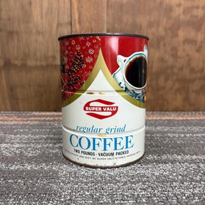以下が含まれることがあります： ヴィンテージのSuper Valuコーヒー缶。缶は円筒形で、赤い上部と白い底部があります。「COFFEE」の文字は青色で、「regular grind」と「TWO POUNDS VACUUM PACKED」と書かれています。缶にはコーヒーカップの写真が描かれています。