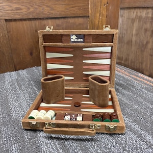 May include: Open backgammon set with a brown corduroy exterior and a brown, tan, and white playing surface. The set includes dice, game pieces, and two brown corduroy dice cups. The brand name "SKOR-MOR" is visible.