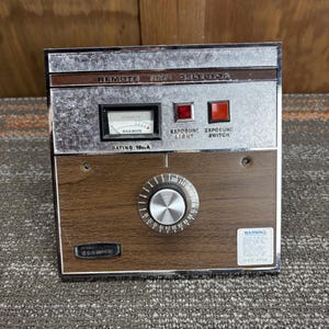 May include: A vintage Remote Time Selector device with a wood grain front panel and a silver top. It features a dial, a meter, and two red switches. The text "REMOTE TIME SELECTOR" is visible.