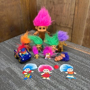 Puede incluir: Una colección de muñecos Troll vintage con pelo puntiagudo y colorido. Los muñecos varían en tamaño y pose, algunos de pie y otros tumbados. También hay un coche de juguete azul y varias pegatinas temáticas de Troll.