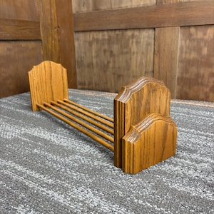 May include: A wooden bookend with a light brown finish. The bookend has a decorative, arched top and four horizontal rods. The bookend is made of solid wood and is designed to hold books upright.