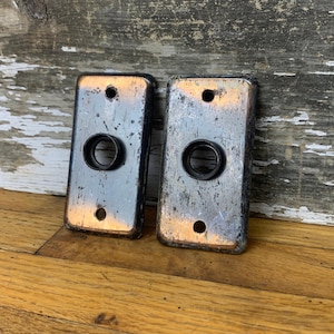 May include: Two vintage metal door plates with a circular hole in the centre. The plates are silver with a copper patina and have a worn, distressed look.