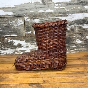 May include: A brown wicker boot-shaped basket. The basket is woven with a natural brown wicker and has a simple design.