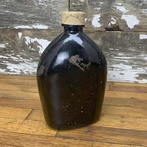 May include: A black glass bottle with a cork top. The bottle has a worn, vintage look with some rust spots on the surface.