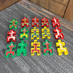 May include: A collection of colorful, vintage clown-shaped puzzle pieces. The pieces are in various colors, including red, green, yellow, and blue. Each piece features a clown design with a painted face and outfit. The puzzle pieces are arranged on a textured surface.