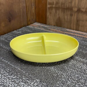 May include: A bright yellow, oval-shaped serving dish with a divider. The dish is made of a smooth, glossy material and is designed to hold two different types of food. The dish is sitting on a gray surface.
