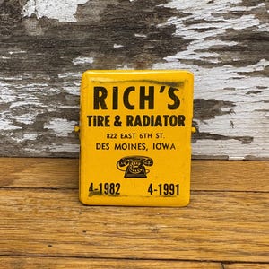 May include: Yellow metal sign with black text advertising Rich's Tire & Radiator. The sign includes the address 822 East 6th St. Des Moines, Iowa and phone numbers 4-1982 and 4-1991.