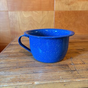 Puede incluir: Una taza de esmalte azul profundo con un patrón de motas blancas en toda la superficie exterior e interior. La taza tiene un borde ancho y redondeado y un asa curva unida al lateral, mostrando un acabado clásico de motas.