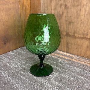 May include: A green glass goblet with a textured surface. The goblet has a wide bowl and a short stem, and it sits on a round base. The glass has a dark green color and a dimpled texture. The goblet is likely used for serving beverages.