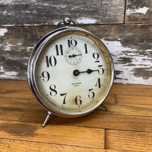 Puede incluir: Un despertador Westclox Big Ben plateado vintage. La esfera del reloj es blanquecina con números y manecillas negras. El reloj tiene una pequeña esfera secundaria en la parte superior y se apoya en dos patas pequeñas.