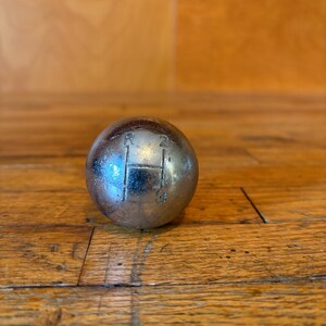 May include: A spherical, metallic gear shift knob with a polished silver finish. The top surface features an engraved H-pattern gear shift diagram with the letters R, 1, 2, and 3 clearly visible, indicating the gear positions for a manual transmission.