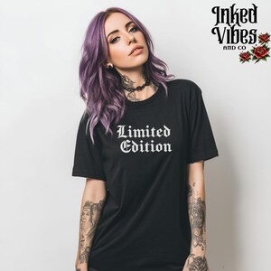 May include: Black t-shirt with the words "Limited Edition" in white gothic font. The image also features the brand name "Inked Vibes and Co" with rose illustrations. The model has purple hair and tattoos.