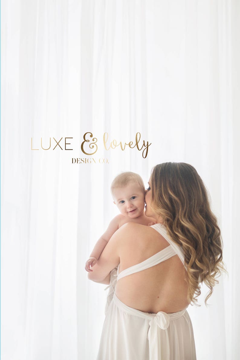 K&ouml;nnte beinhalten: Eine Frau in einem wei&szlig;en Kleid h&auml;lt ein Baby in ihren Armen. Das Baby schaut in die Kamera und l&auml;chelt. Die Frau hat lange, lockige Haare. Der Hintergrund ist ein wei&szlig;er Vorhang. Der Text "LUXE & lovely DESIGN CO." ist im Bild sichtbar.