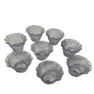 May include: A set of eight clear, seashell-shaped bowls. Each bowl has a wavy, textured rim and a circular base. The bowls are made of a transparent material, allowing light to pass through.
