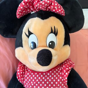 A genuine Disney Parks Minnie Mouse plush from 1992, featuring her signature red bow and polka-dot dress. Softly loved with age, she’s perfect for collectors who cherish authentic park memorabilia.