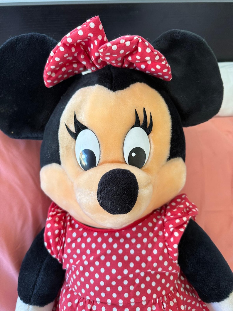 A genuine Disney Parks Minnie Mouse plush from 1992, featuring her signature red bow and polka-dot dress. Softly loved with age, she’s perfect for collectors who cherish authentic park memorabilia.
