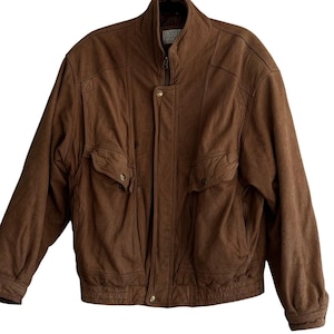 Puede incluir: Chaqueta de cuero marrón con cuello alzado, cierre de cremallera y dos bolsillos delanteros. La chaqueta tiene dobladillo y puños acanalados. La marca "Sculpture Co." es visible en el cuello. Esta chaqueta vintage es una prenda de abrigo clásica.