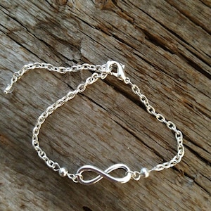 Könnte beinhalten: Ein silbernes Armband mit einem Unendlichkeits-Anhänger, einer zarten Kette und kleinen silbernen Perlen.