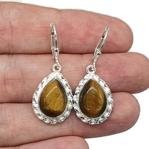 May include: A pair of silver teardrop earrings with brown tiger's eye stones set in a rope-like border.