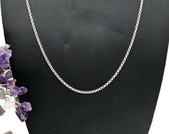 May include: A silver chain necklace on a black velvet display stand. The chain is a simple, delicate design.