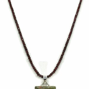 May include: A necklace made of small, dark red beads with a square pendant featuring a green and red stone.