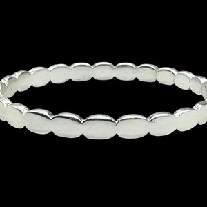 Puede incluir: Un anillo plateado con un dise&ntilde;o ovalado repetido. El anillo, hecho de un material met&aacute;lico brillante, se presenta sobre un fondo negro. Una pieza de joyer&iacute;a sencilla y elegante.