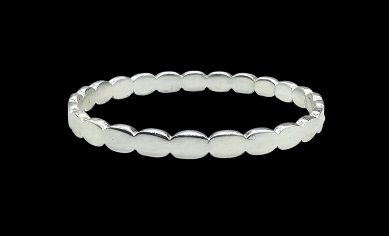 Puede incluir: Un anillo plateado con un dise&ntilde;o ovalado repetido. El anillo, hecho de un material met&aacute;lico brillante, se presenta sobre un fondo negro. Una pieza de joyer&iacute;a sencilla y elegante.