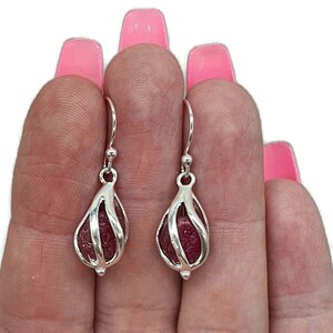 Könnte beinhalten: Ein Paar silberne Ohrhänger mit einem Käfigdesign, in dem sich jeweils ein rosafarbener Rubin befindet.