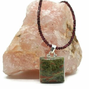 May include: A square green and red jasper pendant hangs from a necklace of dark red garnet beads.