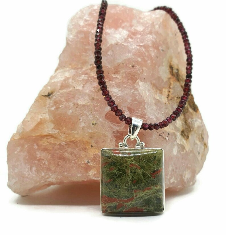 May include: A square green and red jasper pendant hangs from a necklace of dark red garnet beads.
