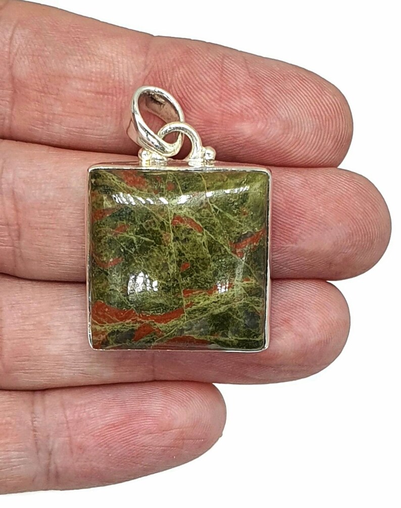 May include: A silver pendant with a square green and red jasper stone. The stone has a swirling pattern of red and green.