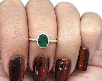 May include: A silver ring with a green oval gemstone. The ring is on a finger with brown nail polish.