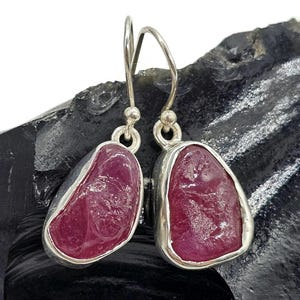 May include: A pair of silver dangle earrings with pink gemstone drops. The gemstones are irregularly shaped and have a rough, natural look.