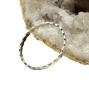 Puede incluir: Un anillo de plata con un dise&ntilde;o de borde festoneado. El anillo es circular y parece estar hecho de un metal brillante. El anillo se muestra sobre un fondo blanco y beige.