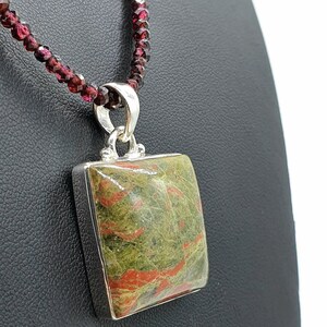 May include: A silver necklace with a square green and red jasper pendant. The necklace is made of small red garnet beads.