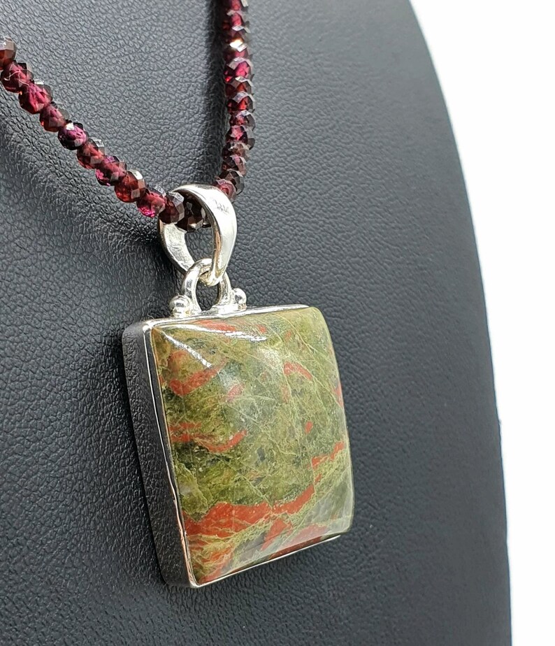 May include: A silver necklace with a square green and red jasper pendant. The necklace is made of small red garnet beads.