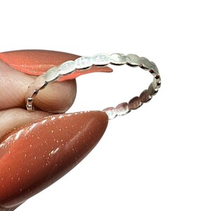 Puede incluir: Un anillo de plata con un dise&ntilde;o delicado de peque&ntilde;as formas ovaladas conectadas. El anillo se muestra sobre un fondo blanco, resaltando su superficie pulida y reflectante. El dise&ntilde;o del anillo es simple y elegante.