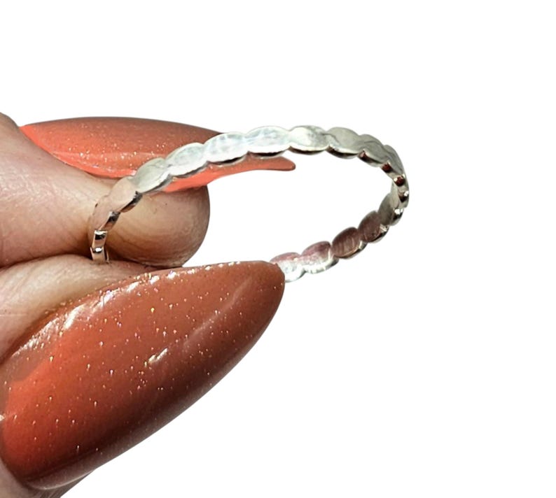 Puede incluir: Un anillo de plata con un dise&ntilde;o delicado de peque&ntilde;as formas ovaladas conectadas. El anillo se muestra sobre un fondo blanco, resaltando su superficie pulida y reflectante. El dise&ntilde;o del anillo es simple y elegante.