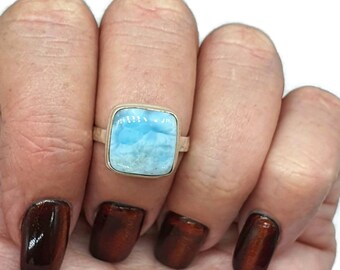 May include: A silver ring featuring a square blue gemstone. The gemstone has a cloudy, marbled pattern.
